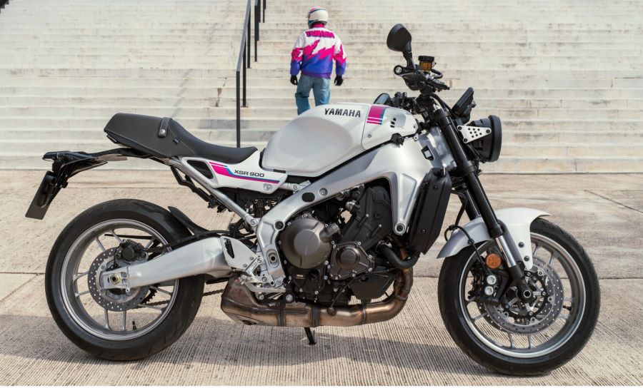 En primer plano, una Yamaha XSR900 2027, detrás un piloto sube por una escalera urbana