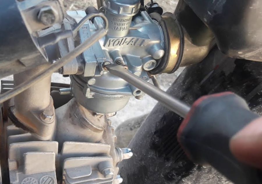Un mecánico trabaja con un destornillador en el carburador de una moto
