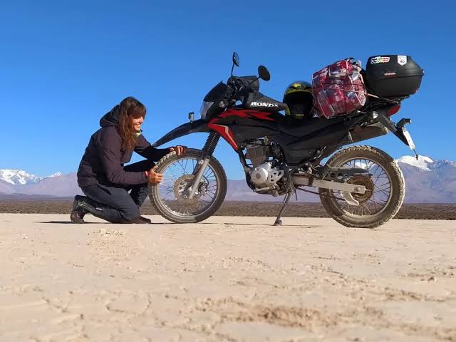 Una motociclista independiente revisa la rueda delantera de su moto offroad cargada de bártulos